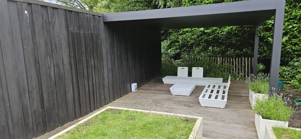 Aluminium terrasoverkapping met vaste wand, ingericht als beschutte loungeplek in de tuin