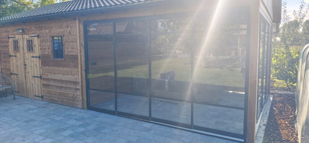 Glazen schuifwand met zwarte steellook profielen geplaatst in een houten bijgebouw in Sint-Gillis-Waas.