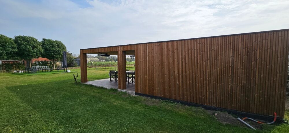 Vrijstaande overkapping met berging in thermowood grenen rib in een tuin in Oostakker