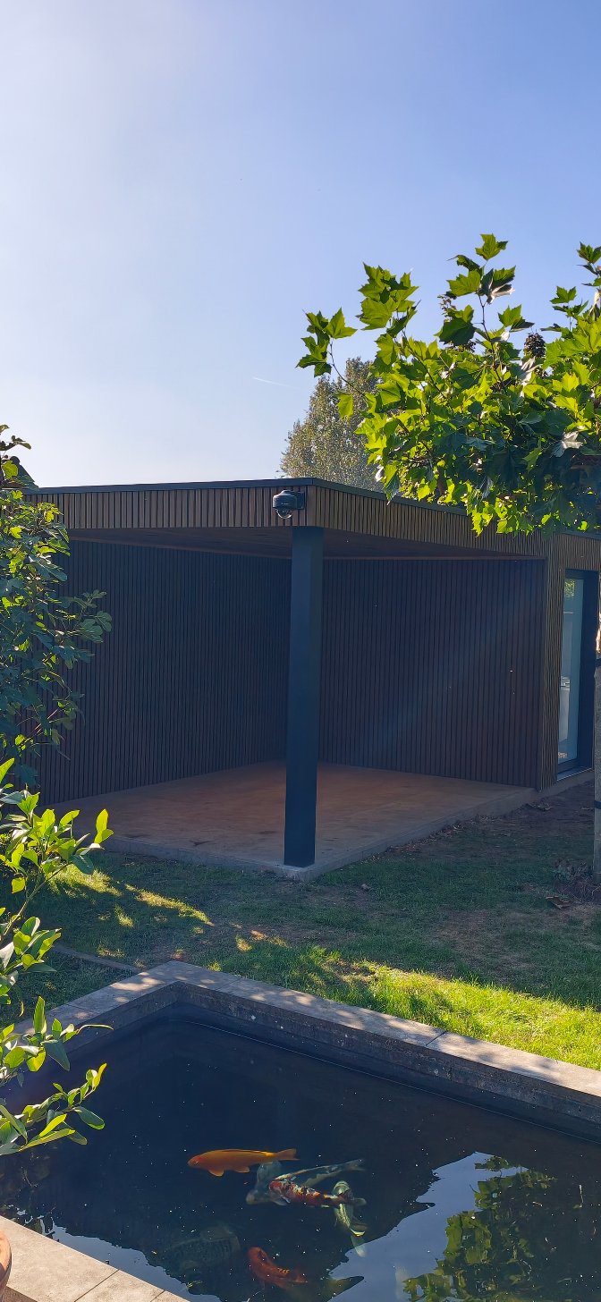 Zicht op de houtlook overkapping en berging vanuit de tuin met zwemvijver